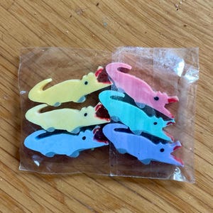 May include: A package of six colorful alligator-shaped erasers. The erasers are in shades of yellow, pink, blue, and green.