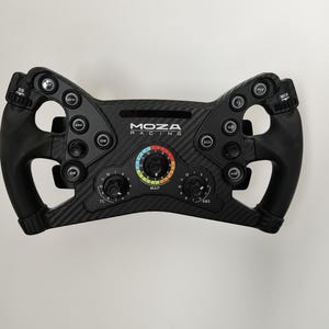 May include: A black racing wheel featuring the "MOZA RACING" logo. The wheel has numerous buttons, dials, and a central display with a colourful gauge. The wheel is made of carbon fibre and has ergonomic grips.
