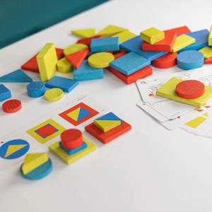 May include: A selection of brightly coloured wooden geometric shapes, including squares, triangles, and circles. The shapes are red, yellow, and blue. Cards with matching patterns are also present. A children's educational toy.