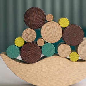 Peut inclure: Un jouet d'équilibre en bois avec une base incurvée et un ensemble de pièces en bois circulaires colorées. Les cercles sont dans des tons de marron, sarcelle, jaune et bois naturel. Le jouet est conçu pour l'empilage et l'équilibre.