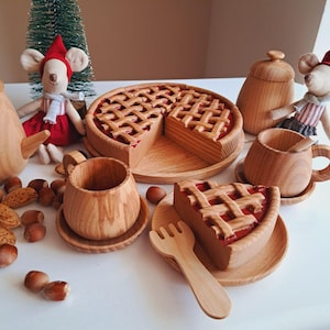 Op de afbeelding: Houten speelgoedset met een taart met een rasterkorst, een stuk taart, kopjes, schotels, een suikerpot en een vork. De taart heeft een rode vulling. De set bevat twee muizenpoppen in rood-witte outfits.