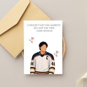 Puede incluir: Una tarjeta de felicitación blanca con la ilustración de una persona de pelo oscuro rizado que viste una camiseta de hockey blanca, azul marino y amarilla con el número 44 y una C. El texto dice I COULDN'T GET YOU GARRETT, SO I GOT YOU THIS CARD INSTEAD.