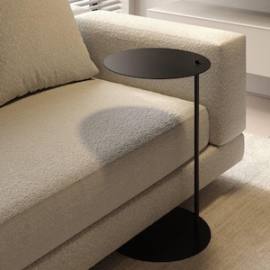 May include: A black side table with a round top and a single, slender leg. The table is next to a beige couch.