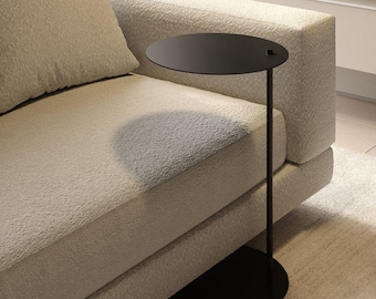 May include: A black side table with a round top and a single, slender leg. The table is next to a beige couch.