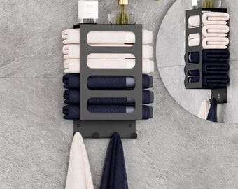 May include: A black metal towel rack on a grey tiled wall, holding folded white and navy blue towels. The rack has a shelf with decorative items and hooks for hanging towels. A mirror reflects the rack.