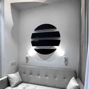 May include: A modern black wall shelf with a circular design, featuring four horizontal shelves. The shelves are mounted on a white wall above a gray sofa. Two small wall sconces are positioned below the shelf.