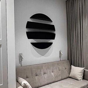 May include: A modern living room scene featuring a black, semi-circular wall shelf arrangement. The shelves are mounted on a light gray wall above a beige sofa with a matching pillow. A gray curtain hangs on the right.