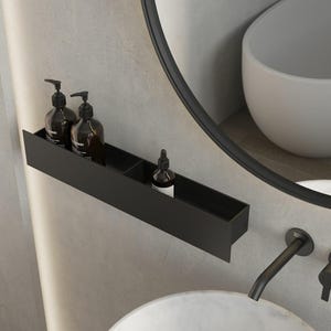 May include: A matte black rectangular wall-mounted shelf featuring two distinct compartments. The shelf holds two dark amber pump bottles and one small dropper bottle with a black cap, providing organized storage for bathroom essentials.