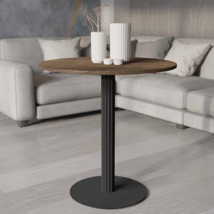 May include: A round side table with a dark brown wooden top and a black metal base. The base has a cylindrical design with vertical grooves. Two white vases and two small white bowls sit on the table. The table is 24 inches in diameter.