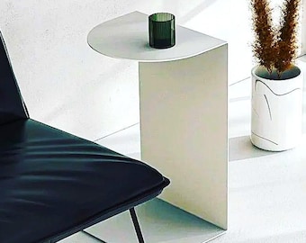 May include: A white side table with a curved top and a single leg. The table is made of metal and has a modern design. A green glass candle holder sits on the table.