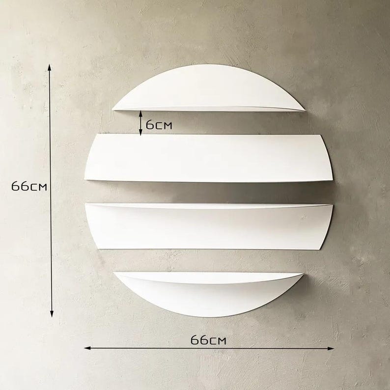 May include: White, semi-circular wall shelves arranged in a circular pattern. The shelves are 66 cm wide and 66 cm high, with a depth of 6 cm. The shelves are mounted on a gray wall. The design is modern and minimalist.