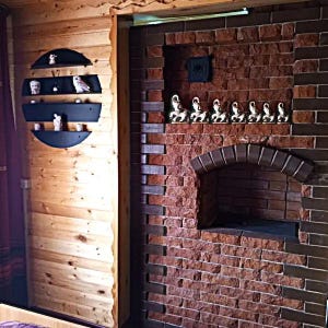 May include: Interior shot of a rustic room with a brick wall and wooden paneling. A series of small owl figurines are displayed on a black, semi-circular shelf. The brick wall features a small arched opening and a row of decorative figurines.