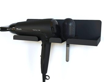 Puede incluir: Un soporte negro para secador de pelo montado en la pared con un secador de pelo Philips y un cepillo. El soporte tiene un estante para el secador de pelo y un compartimento separado para el cepillo. El secador de pelo es negro con el texto "Philips ThermoProtect 2100W".