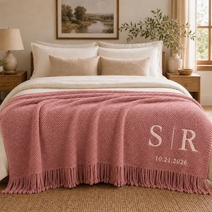 Könnte beinhalten: Eine altrosa gestrickte Wohndecke mit texturiertem Waffelmuster und langen Fransen an der Unterkante. Die Decke ist mit den weiß gestickten Buchstaben S und R personalisiert, die durch eine vertikale Linie getrennt sind, mit 10.21.2026 darunter.