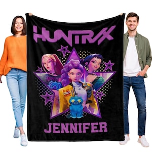 Puede incluir: Manta negra con el texto morado "HUNTRAX" y un gr&aacute;fico de tres mujeres animadas dentro de una estrella. La palabra "JENNIFER" est&aacute; impresa en morado en la parte inferior. Tambi&eacute;n aparece un gato azul en el gr&aacute;fico.