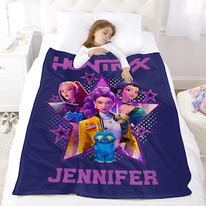 Puede incluir: Una manta azul marino con un gr&aacute;fico de tres mujeres animadas y un gato azul, con el texto "HUNTIX" y "JENNIFER" en morado. La manta est&aacute; sobre una cama con una persona durmiendo.