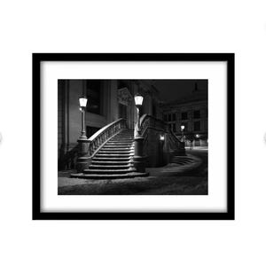 May include: Black and white framed print of a snow-covered outdoor staircase at night. The staircase has ornate railings and is lit by street lamps. The print is in a black frame.