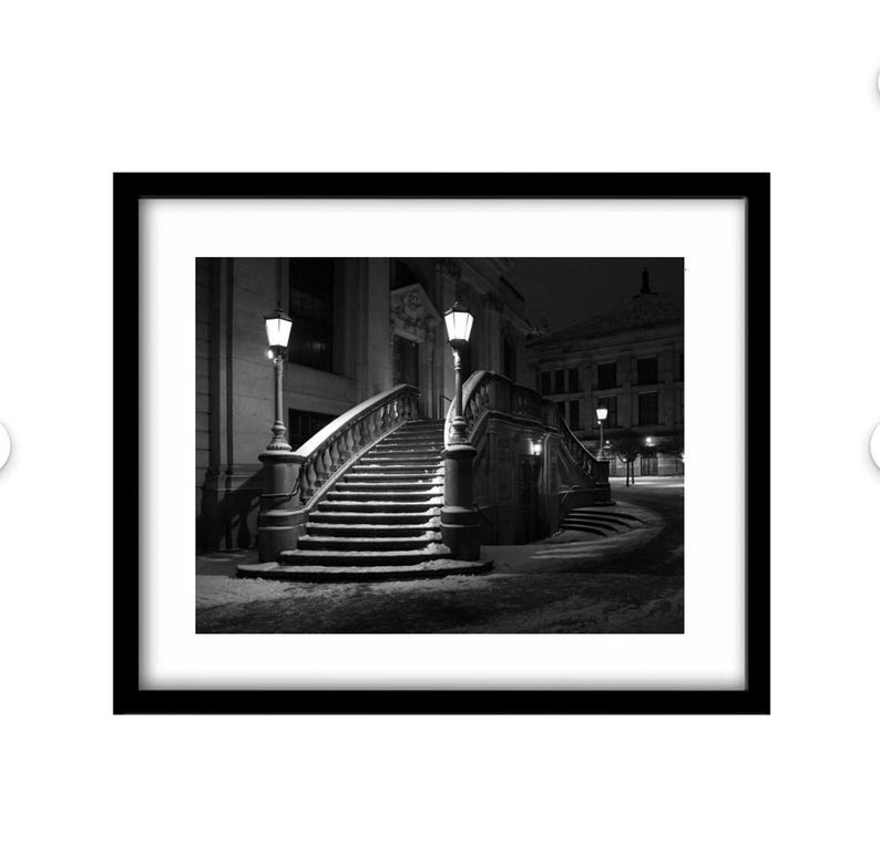 May include: Black and white framed print of a snow-covered outdoor staircase at night. The staircase has ornate railings and is lit by street lamps. The print is in a black frame.