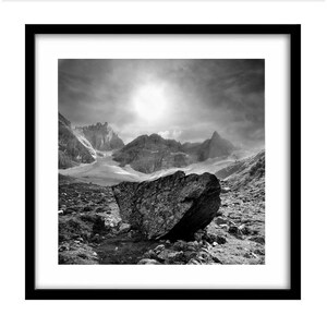 May include: Black and white framed print of a mountain landscape. A large boulder sits in the foreground, with mountains and a cloudy sky in the background. The print is in a black frame.