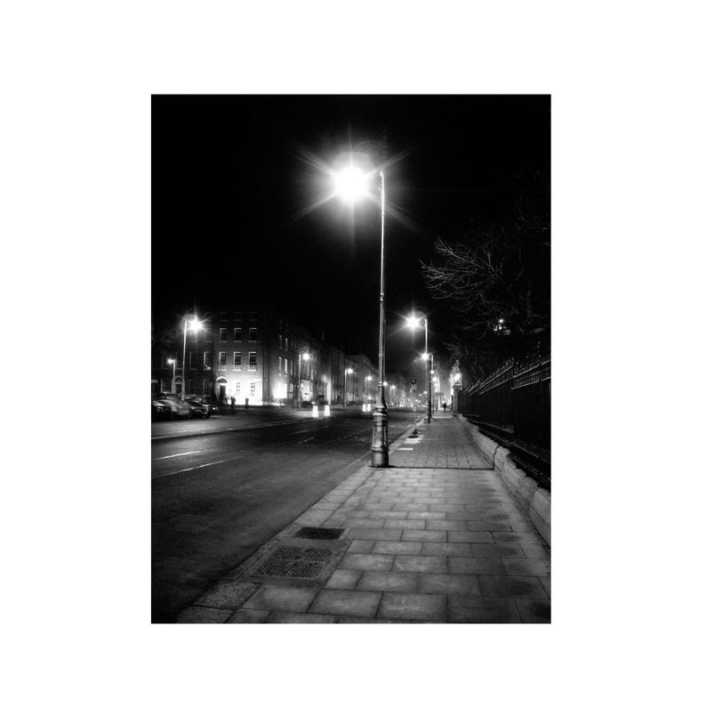Black and white picture of street lights illuminating the empty surrounding street with slabbed footpath in Dublin city, Ireland.