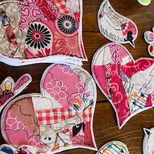 May include: A collection of handmade fabric hearts and birds. The hearts are made of patchwork fabric in shades of pink, red, and white. The birds are made of patchwork fabric in shades of blue, white, and green.