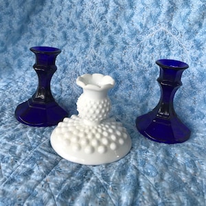 May include: Three candle holders, two are blue glass and one is white milk glass with a textured surface.