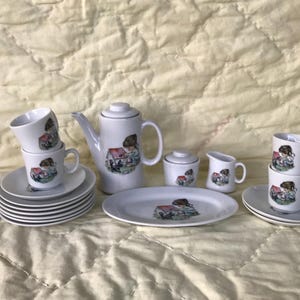 May include: A white tea set with a floral design featuring a girl and a house. The set includes a teapot, creamer, sugar bowl, and four teacups and saucers.