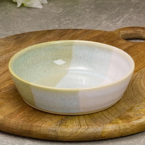 Peut inclure: Un bol rond en céramique avec un design de couleur segmenté vert, blanc et jaune. Le bol est posé sur une planche à découper en bois avec une poignée. Le bol a une finition lisse et brillante.