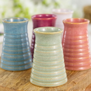 May include: Five ceramic vases in shades of blue, green, red, pink, and white. Each vase features a ribbed pattern and a gently widening top. They are displayed on a wooden chopping board.