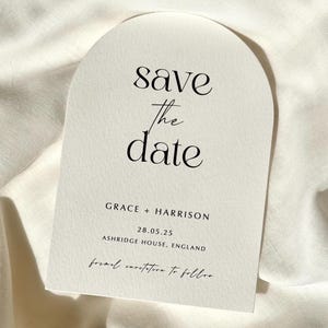 Pode incluir: Um cartão arqueado creme com o texto "save the date" em escrita preta. Inclui os nomes "GRACE + HARRISON", a data "28.05.25" e "ASHRIDGE HOUSE, ENGLAND". A parte inferior diz "formal invitation to follow".