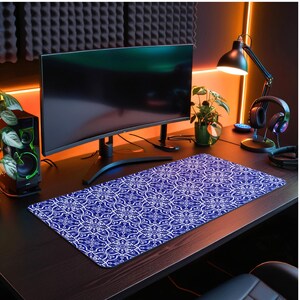 May include: A blue and white patterned mouse mat with a geometric design. The mouse mat is on a dark wood desk with a computer monitor, a speaker, and a plant.