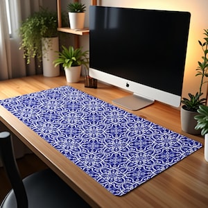May include: A blue and white patterned desk mat with a geometric design. The mat is on a wooden desk with a computer monitor on the desk.