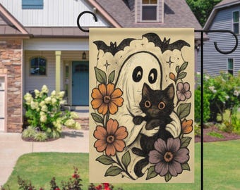 Peut inclure: Un drapeau de jardin d'Halloween avec une illustration vintage. Il représente un fantôme amical tenant un chat noir, entouré de fleurs orange, violettes et roses, avec des chauves-souris en haut. Le drapeau est affiché dans un jardin.