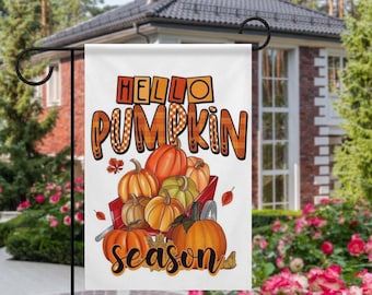 May include: A white garden flag with the words "Hello Pumpkin Season" in orange and brown lettering. The flag features a red wagon filled with pumpkins in various shades of orange and green, ideal for autumn decor.