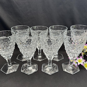 May include: A set of eight clear glass goblets featuring a textured hobnail pattern on the bowl, a short stem, and a hexagonal base. The glasses are arranged in a group, showcasing the repeating geometric indentations across the surface of each.