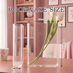 May include: Two clear rectangular book-shaped vases. One vase contains two white artificial tulips with green stems. The image includes text reading BOOK VASE SIZE and dimensions: 15cm/5.9 inches wide, 20cm/7.9 inches high, and 4cm/1.6 inches deep.