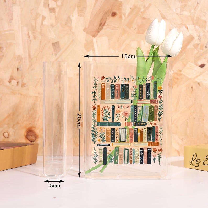 Pode incluir: Um vaso retangular transparente com um design de estante, com 20 cm de altura, 15 cm de largura e 5 cm de profundidade. O vaso cont&eacute;m tulipas brancas. O design da estante apresenta livros coloridos e detalhes florais.