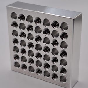 May include: A rectangular, silver-colored metal block with a grid of evenly spaced, circular holes. Each hole has a threaded interior. The block has a smooth, brushed finish and is set against a plain background.