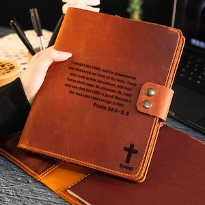 May include: A brown leather journal with a cross and the name "Daniel" engraved on the front. The journal has a strap closure with two metal studs. Text from Psalm 34:4-5, 8 is also engraved on the cover.