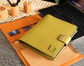 May include: A green leather bound journal with a personalized inscription that reads "L Linda". The journal is open to reveal a blank page and is sitting on top of a brown leather folder.