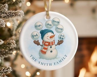 May include: A white ceramic Christmas ornament featuring a snowman with a blue hat, carrot nose, and red and white scarf. The ornament has the text "The Smith Family" and names like "Mum", "Dad", "Jess", "Henry", "Harry", and "Bob".