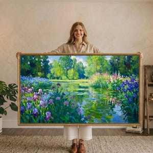 May include: A framed landscape painting depicting a serene pond scene with vibrant purple and blue irises, lush green trees, and reflections in the water. The artwork is encased in a gold-colored frame.