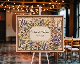 May include: A rectangular wedding sign on a wooden easel featuring a stained glass style border of colorful wildflowers including lavender, daisies, and lilies. The center panel is cream colored with the text Oliver & David and 06.09.2026.