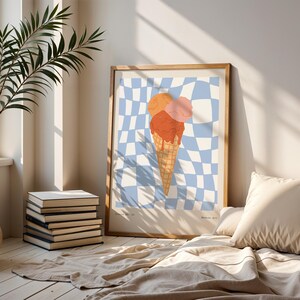 May include: A framed art print featuring an ice cream cone with three scoops in orange and pink hues, set against a blue and white checkered background. The artwork is displayed in a light-colored wooden frame, adding a touch of warmth to the room's decor.