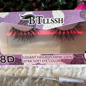 K&ouml;nnte beinhalten: Eine violette und wei&szlig;e Schachtel mit einem Paar k&uuml;nstlicher Wimpern in einem transparenten Fenster. Die Schachtel tr&auml;gt die Aufschrift "BTLLSSH 8D ELEGANT FASHION MINK 100% EXTRA SOFT EYE COLOR" und "100% SUPER NATURAL".