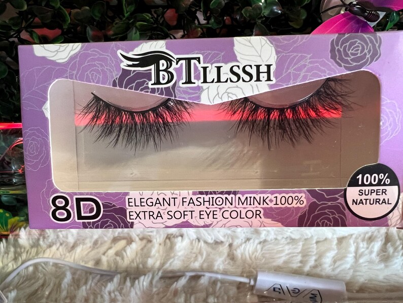 K&ouml;nnte beinhalten: Eine violette und wei&szlig;e Schachtel mit einem Paar k&uuml;nstlicher Wimpern in einem transparenten Fenster. Die Schachtel tr&auml;gt die Aufschrift "BTLLSSH 8D ELEGANT FASHION MINK 100% EXTRA SOFT EYE COLOR" und "100% SUPER NATURAL".