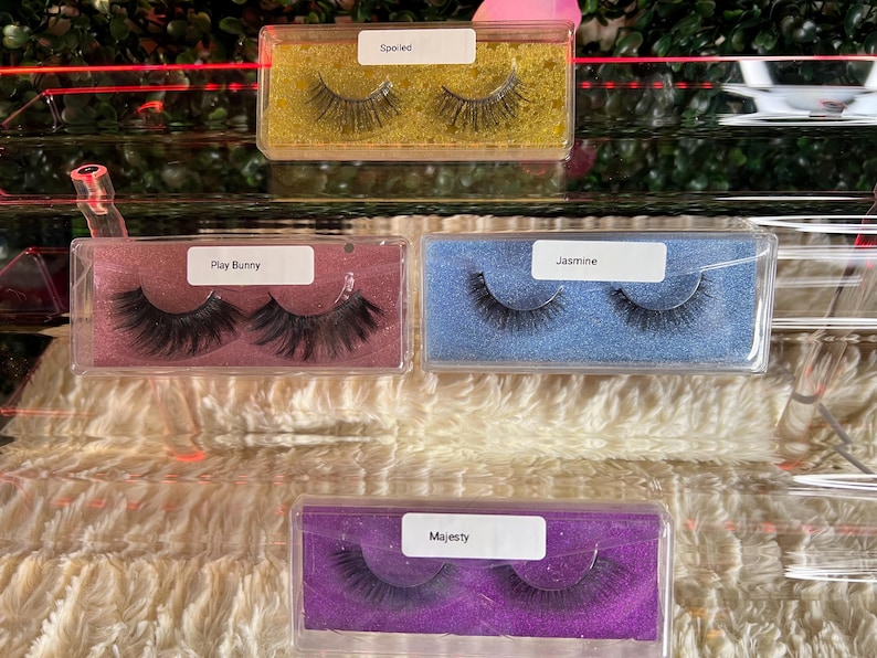 K&ouml;nnte beinhalten: Vier transparente Plastikboxen mit verschiedenen Hintergrundfarben und falschen Wimpern darin. Die Boxen sind mit "Spoiled", "Play Bunny", "Jasmine" und "Majesty" beschriftet.