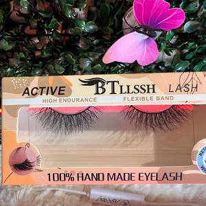 K&ouml;nnte beinhalten: Nahaufnahme einer Packung mit falschen Wimpern. Die Verpackung ist rosa und wei&szlig; mit dem aufgedruckten Text "ACTIVE BTLLSSH LASH HIGH ENDURANCE FLEXIBLE BAND 100% HAND MADE EYELASH". Die Wimpern sind schwarz und haben einen 3D-Schwung. Die Verpackung hat auch einen kleinen Aufkleber mit der Aufschrift "RETAINS 3D CURL WHEN WET".