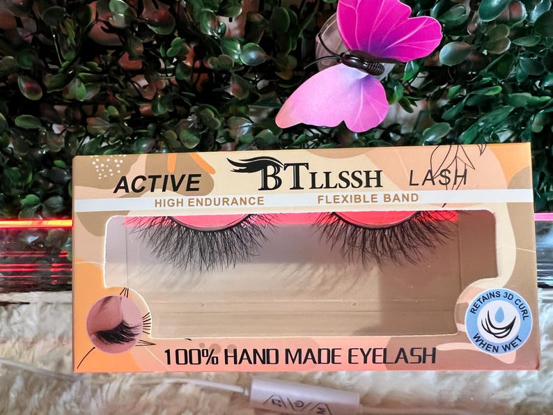 K&ouml;nnte beinhalten: Nahaufnahme einer Packung mit falschen Wimpern. Die Verpackung ist rosa und wei&szlig; mit dem aufgedruckten Text "ACTIVE BTLLSSH LASH HIGH ENDURANCE FLEXIBLE BAND 100% HAND MADE EYELASH". Die Wimpern sind schwarz und haben einen 3D-Schwung. Die Verpackung hat auch einen kleinen Aufkleber mit der Aufschrift "RETAINS 3D CURL WHEN WET".