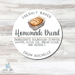 May include: A round white sticker with the text "FRESHLY BAKED Homemade Bread." The sticker features a watercolor illustration of a loaf of bread in a baking pan. Ingredients listed: sourdough starter, water, olive oil, bread flour, and sea salt.